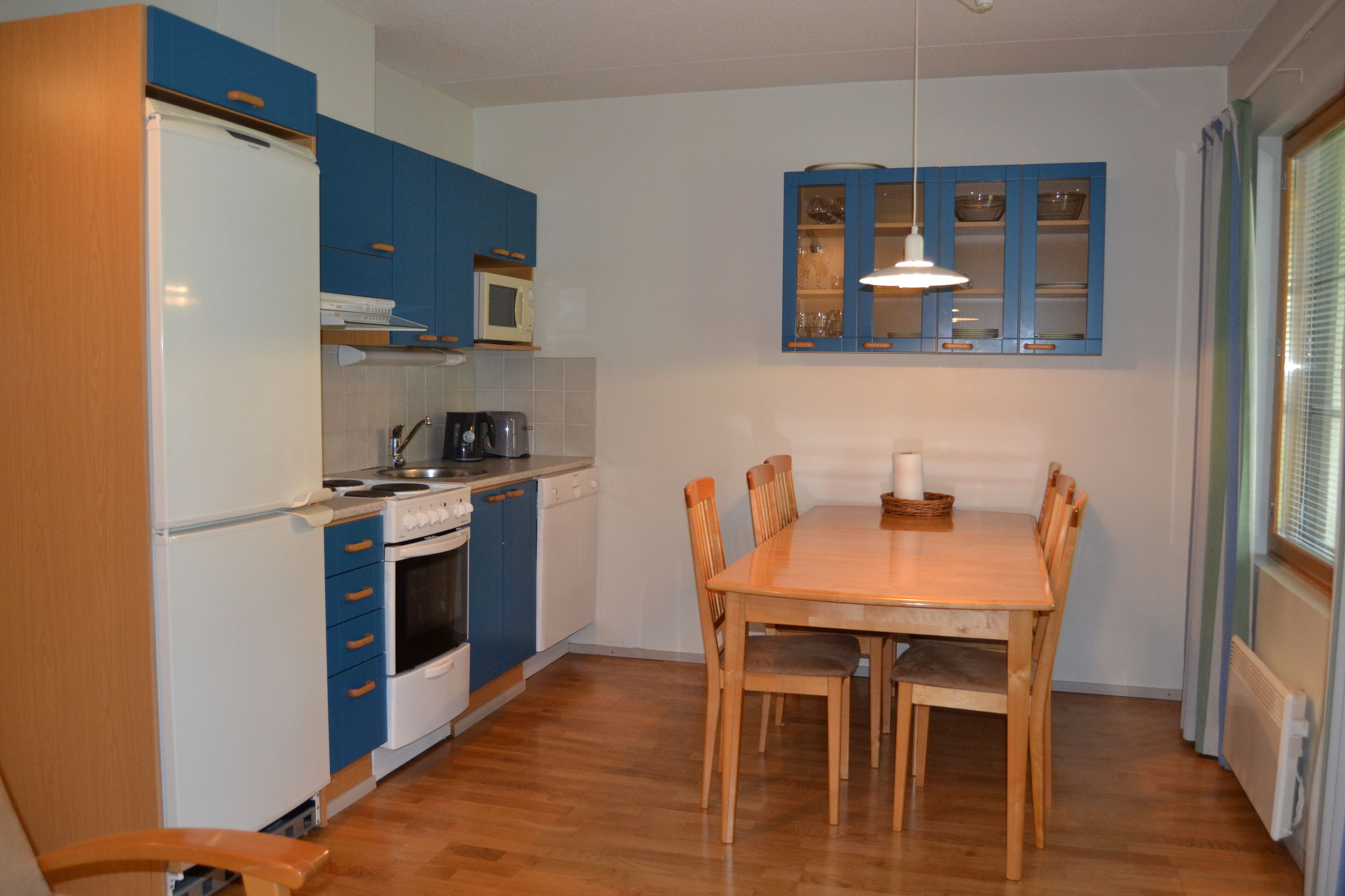 Una cocina funcional con armarios azules, una mesa de comedor de madera y una ventana con persianas.
