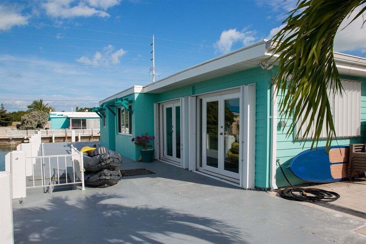 A turquoise building with a covered outdoor area, a white fence, and a surfboard.