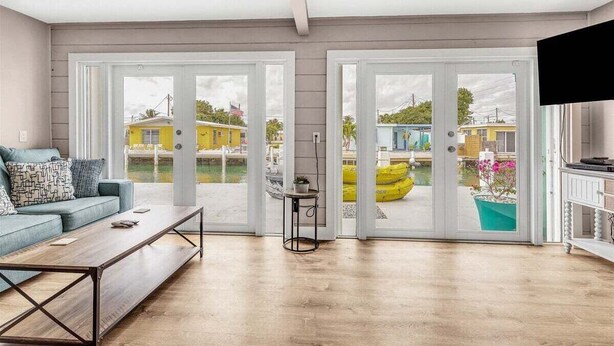 A spacious living room with a large sliding glass door leading to a pool area, a comfortable sofa, and a flat-screen TV. - Reel Deal ~ Private Pool Home, 76' Dock (Marathon)