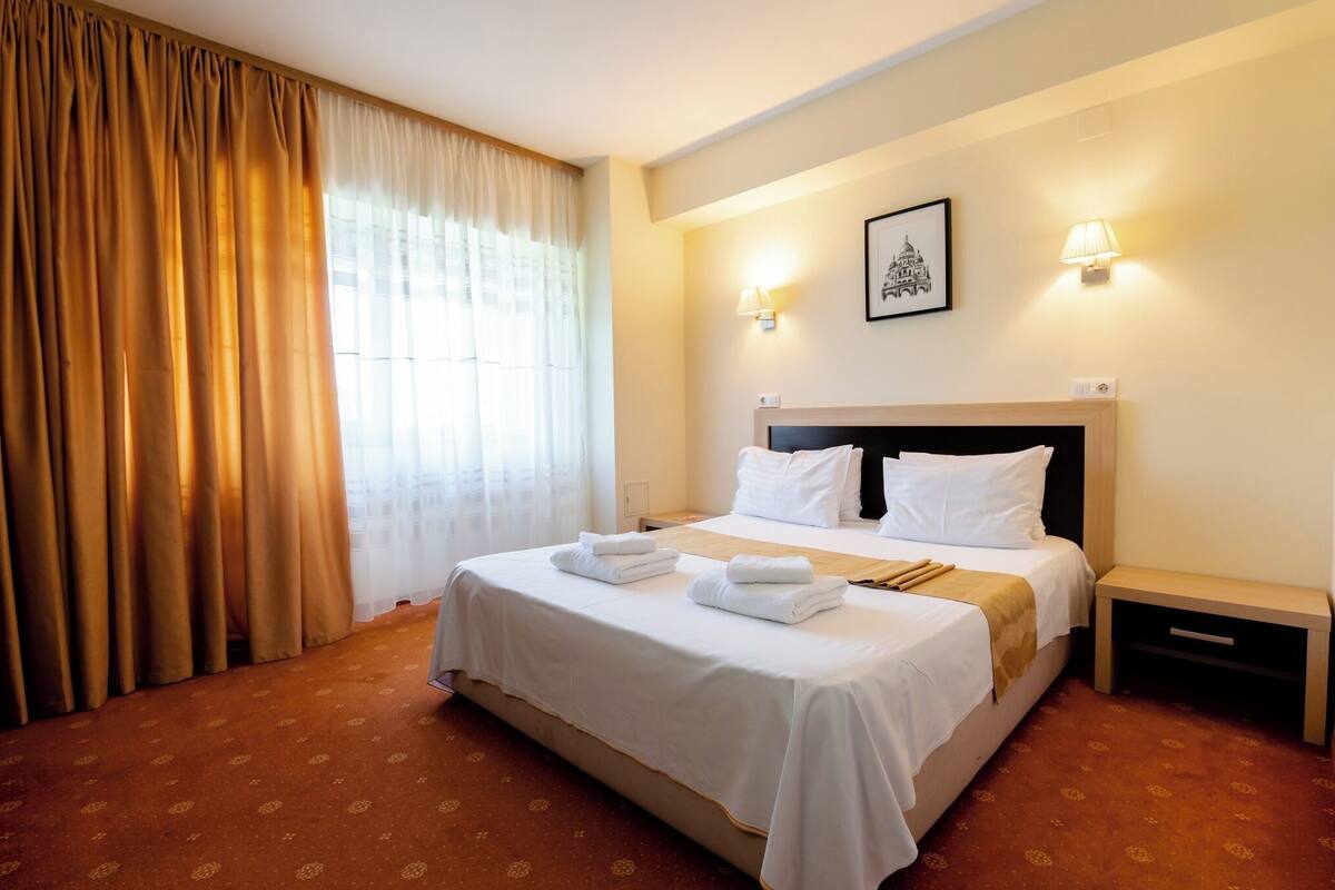 A hotel room with a bed, two bedside tables, a nightstand, a lamp, and a framed picture on the wall.