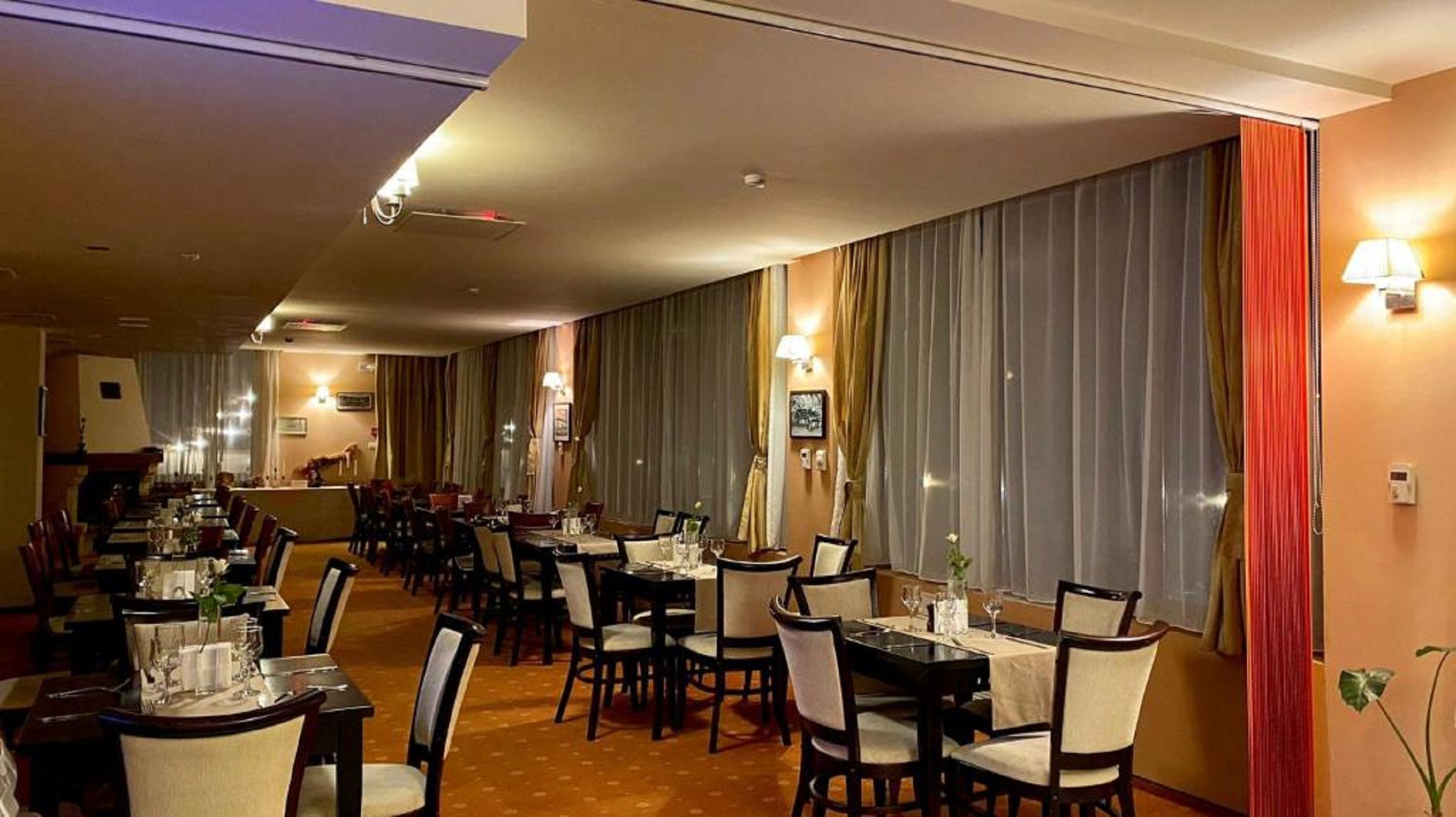 A hotel dining area with multiple tables and chairs, a long counter, and a view of the street through large windows.