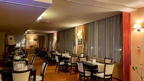 A hotel dining area with multiple tables and chairs, a long counter, and a view of the street through large windows. - Hotel Oxford Inns & Suites (Timisoara)
