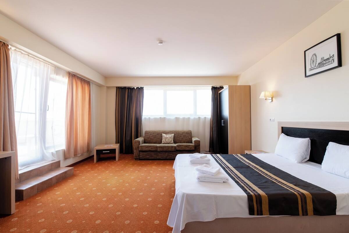 A hotel room with a bed, a sofa, a small table, and a window with curtains.