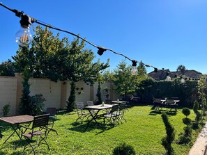 Un patio al aire libre con mesas y sillas, luces colgantes y un cielo azul despejado.
