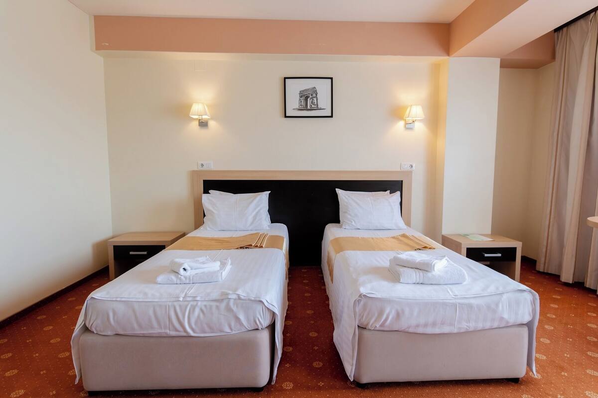 A hotel room with two single beds, a large bed frame, bedside tables, wall-mounted lamps, and a framed picture on the wall.