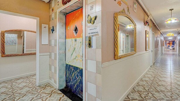A hallway with a tiled floor, a door with a colorful abstract mural, and a mirror on the wall.