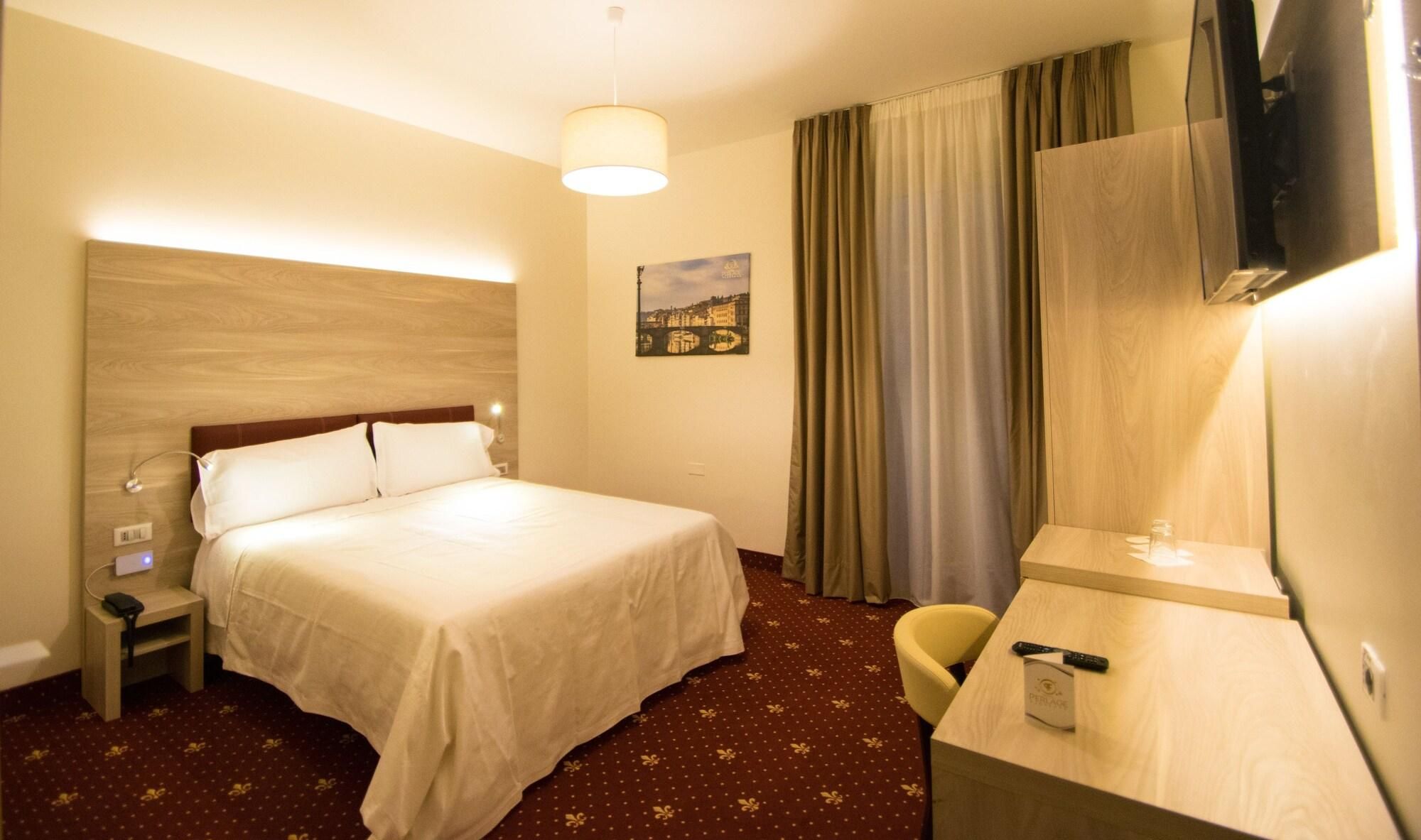 A hotel room with a bed, bedside table, lamp, chair, desk, and a television.