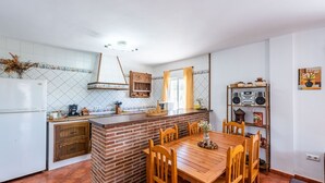 A kitchen with a brick island, wooden cabinets, and a dining table with chairs. - Chalet Algar by Ruralidays (Cádiz)