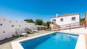 A swimming pool with a white house in the background, a wooden fence, and a clear blue sky. - Chalet Algar by Ruralidays (Cádiz)