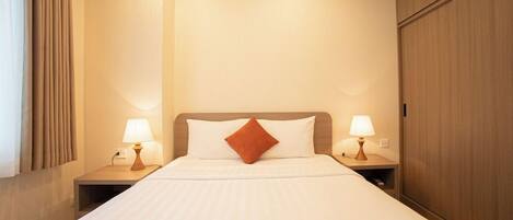 A hotel room with a bed, two bedside lamps, a wooden wardrobe, and a window with curtains.