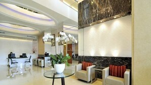 Een moderne hotellobby met een receptiebalie, een zithoek en een grote kamerplant.