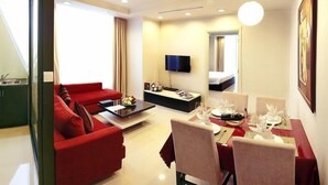 Een compacte hotelkamer met een rode bank, een eettafel gedekt voor twee personen, een flatscreen televisie en een kleine kitchenette.