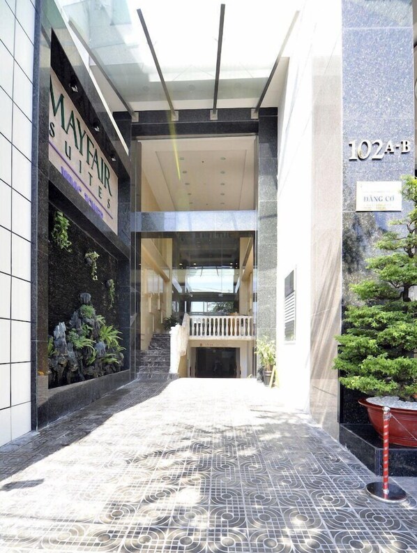 Een hotelingang met een betegelde vloer, een trap en een bordje met 'MAYFAIR SUITES'.