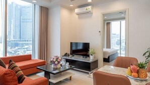 Een moderne hotelkamer met een groot raam, een flatscreen televisie, een bank, een eettafel met fruit en een bed.