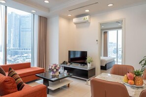 Een moderne hotelkamer met een groot raam, een flatscreen televisie, een bank, een eettafel met fruit en een bed.