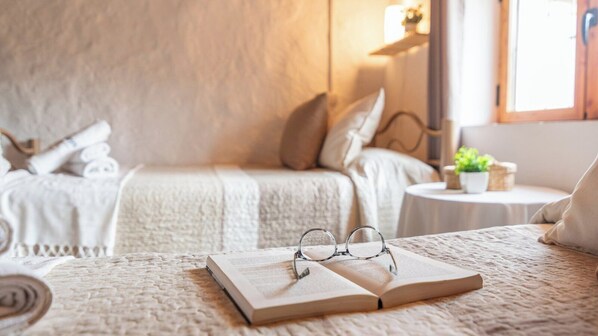 A cozy bedroom with a large bed, a smaller bed, and a bedside table with a plant.