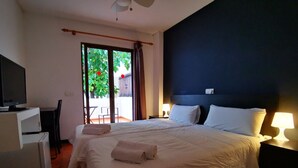 A hotel room with a bed, a desk with a computer, a chair, a TV, and a balcony with a view of greenery. - Hostal Balearic (Sant Antoni de Portmany)