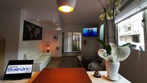 A modern hotel room with a white sofa, a desk with a laptop, a potted orchid, and a TV on the wall. - Hostal Balearic (Sant Antoni de Portmany)