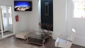 A modern living room with a glass coffee table, a sofa, a TV mounted on the wall, and a door with a mirror. - Hostal Balearic (Sant Antoni de Portmany)