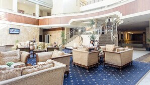 A spacious lobby with multiple seating areas, a central staircase, and a view of the upper floor.