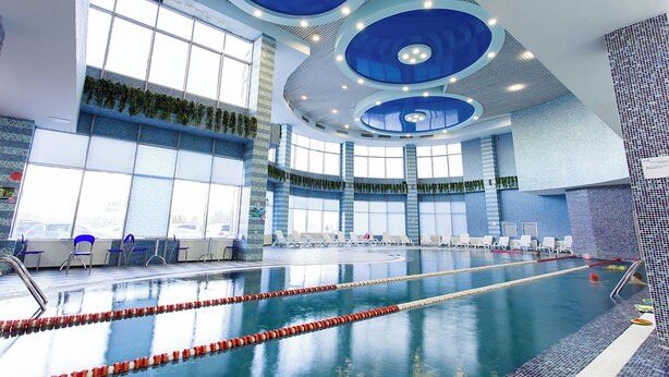 An indoor swimming pool with multiple lanes, large windows, and a modern ceiling design.