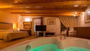 Una habitación con una bañera grande, una cama, un televisor y techo de madera.