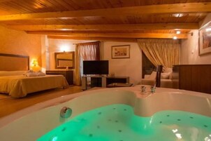 Una habitación con una bañera grande, una cama, un televisor y techo de madera.
