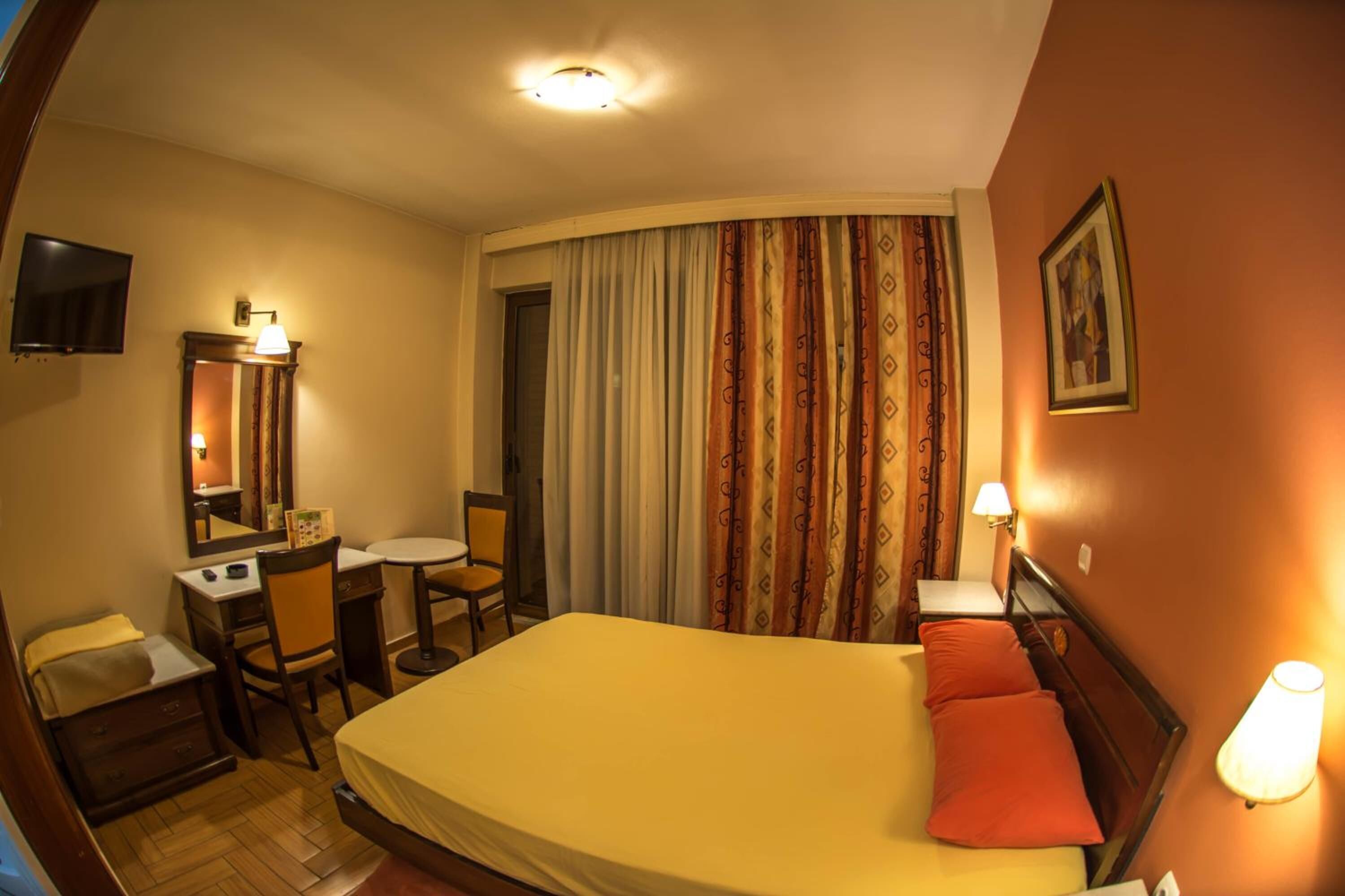 A hotel room with a bed, a desk, a chair, a television, and a window with curtains.