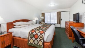 Habitación de hotel con cama, escritorio, silla, televisor y ventana con cortinas.