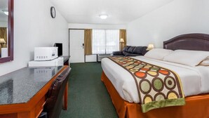 Habitación de hotel con cama, escritorio, silla, microondas, reloj y ventana con cortinas.