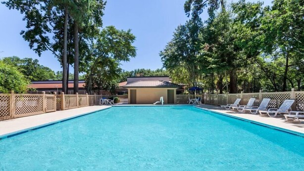 Una piscina rectangular con superficie de agua azul cristalina, rodeada por una valla de madera y protegida por árboles.