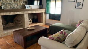 Un saló amb una llar de pedra, una taula de centre de fusta i un sofà beix amb coixinets florals.