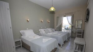 A hotel room with two beds, a small table, a wardrobe, and a window with curtains.