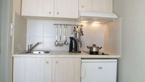 A compact kitchen with white cabinets, a sink, a kettle, and a small refrigerator.