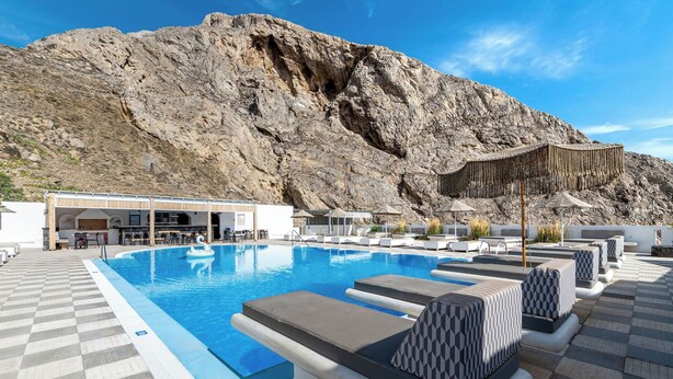 A pool area with lounge chairs, a bar, and a mountain backdrop. - Marianna Hotel (Santorini)