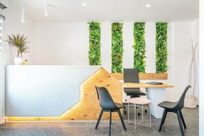 A reception desk with a wooden accent, two black chairs, a small round table, and vertical green plant walls. - Marianna Hotel (Santorini)