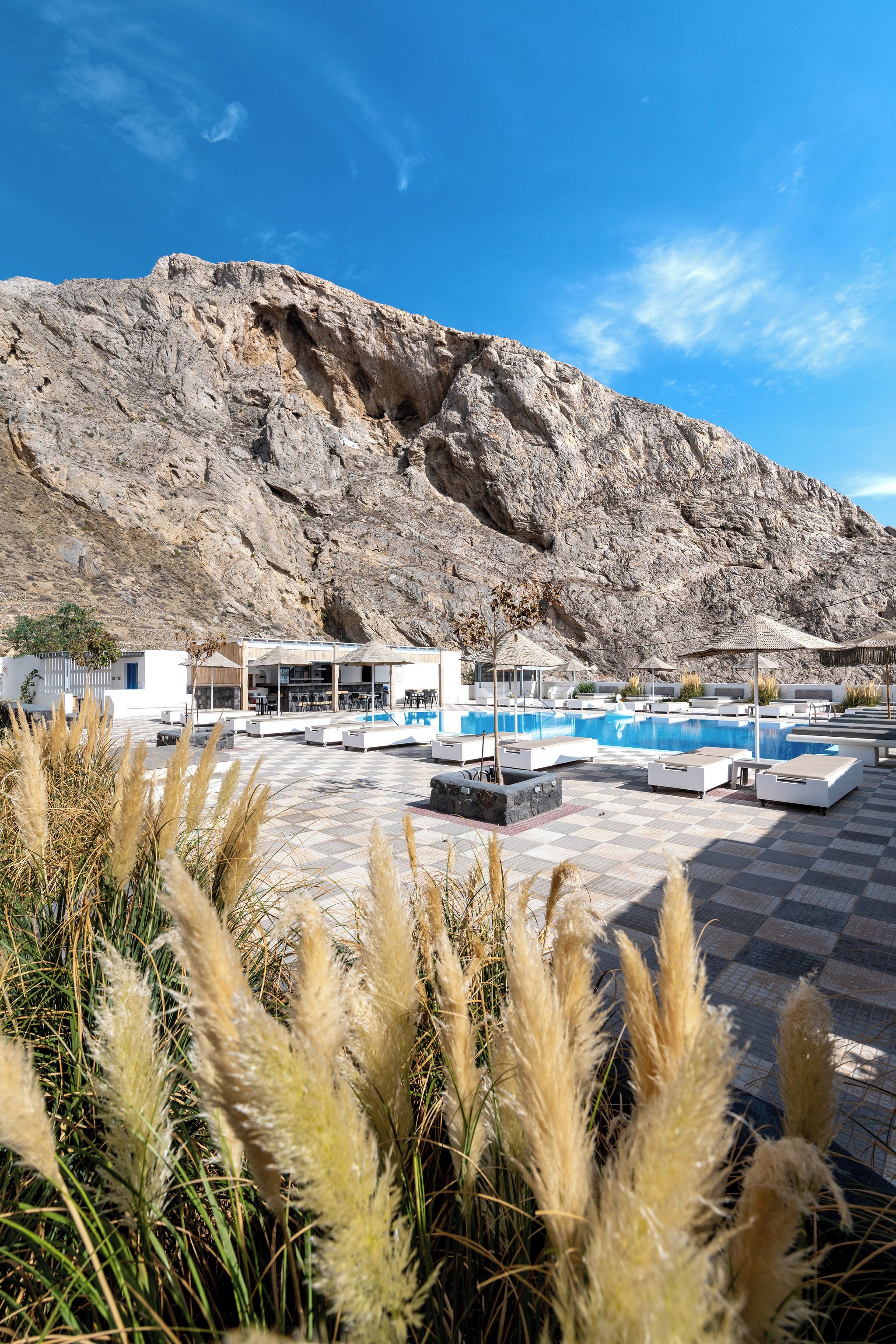 A pool area with lounge chairs and umbrellas, a rocky mountain backdrop, and a checkered floor.