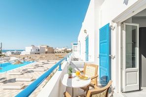 A balcony with a pool, a table with a chair, and a door. - Marianna Hotel (Santorini)