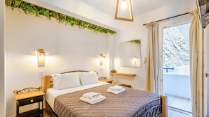 A bedroom with a bed, bedside tables, a nightstand, a mirror, and a view of a balcony. - Marianna Hotel (Santorini)