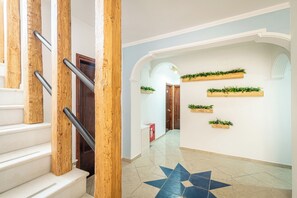 Eine Treppe mit Holzhandläufen, einem gefliesten Boden mit Sternenmuster und an den Wänden bepflanzte Holzbehälter mit Grünpflanzen.