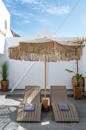 Two wooden lounge chairs with towels, a woven umbrella, and potted plants on a rooftop terrace. - Marianna Hotel (Santorini)