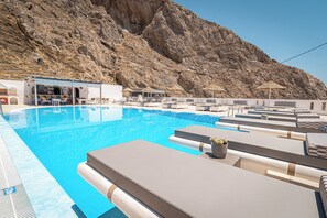 A pool area with lounge chairs, a bar, and a mountainous backdrop. - Marianna Hotel (Santorini)