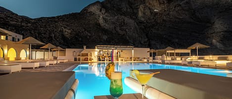 Zona junto a la piscina con sillones de descanso y un bar, con vistas a un paisaje montañoso.