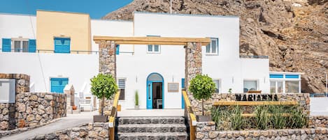 A building with a stone facade, a wooden pergola entrance, and a sign indicating it is a hotel.