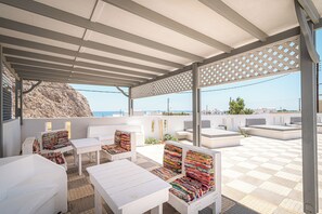 Ein überdachter Außenbereich mit weißen Möbeln und Blick auf das Meer.