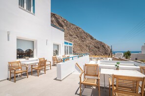 A terrace with wooden chairs and a table, overlooking a rocky landscape and the sea. - Marianna Hotel (Santorini)