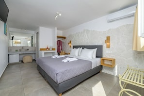 A modern bedroom with a large bed, a bedside table, a small bedside lamp, and a wall-mounted air conditioner. - Marianna Hotel (Santorini)