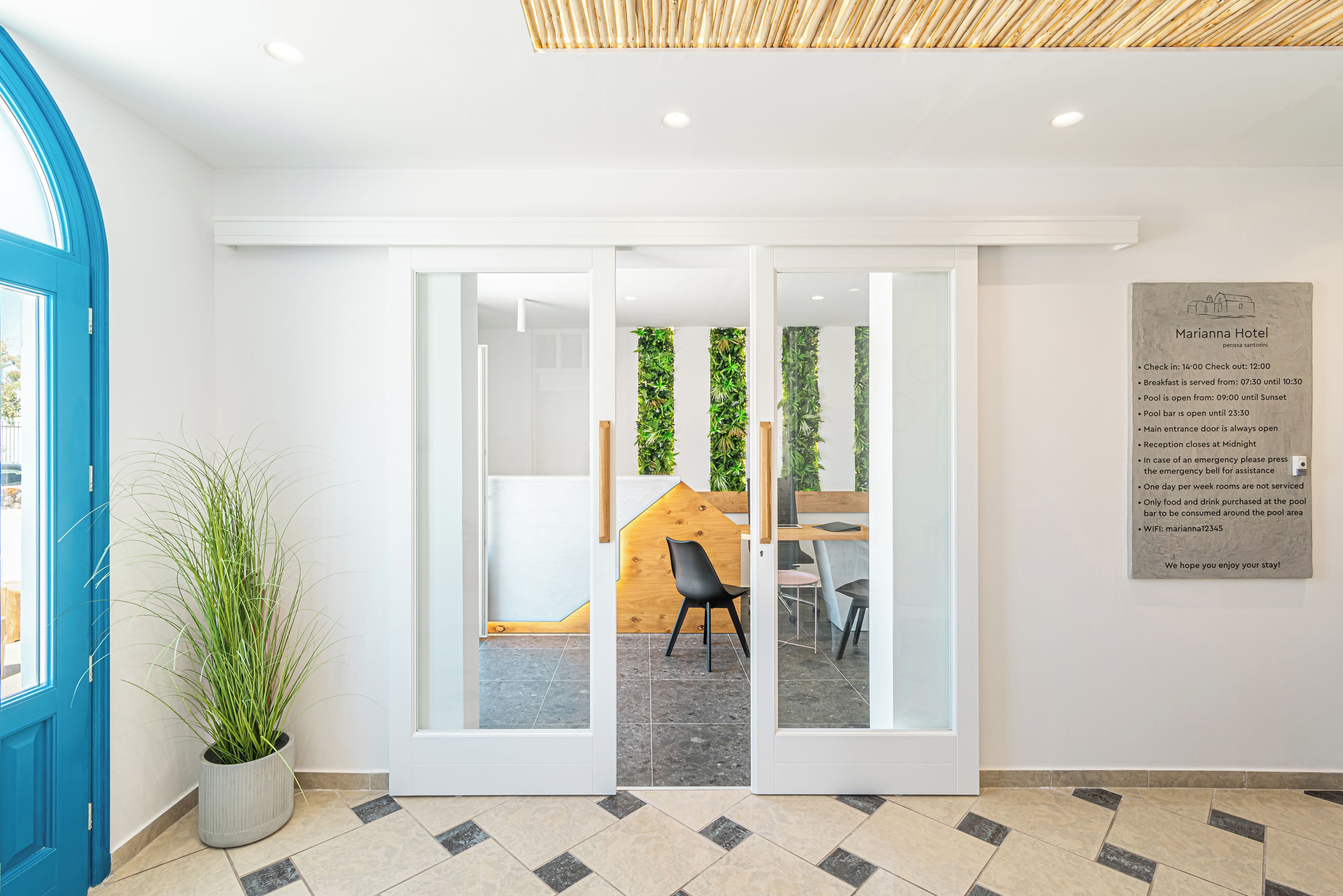 Una recepción de hotel moderna con puerta de vidrio, una planta en maceta y un panel decorativo de madera.