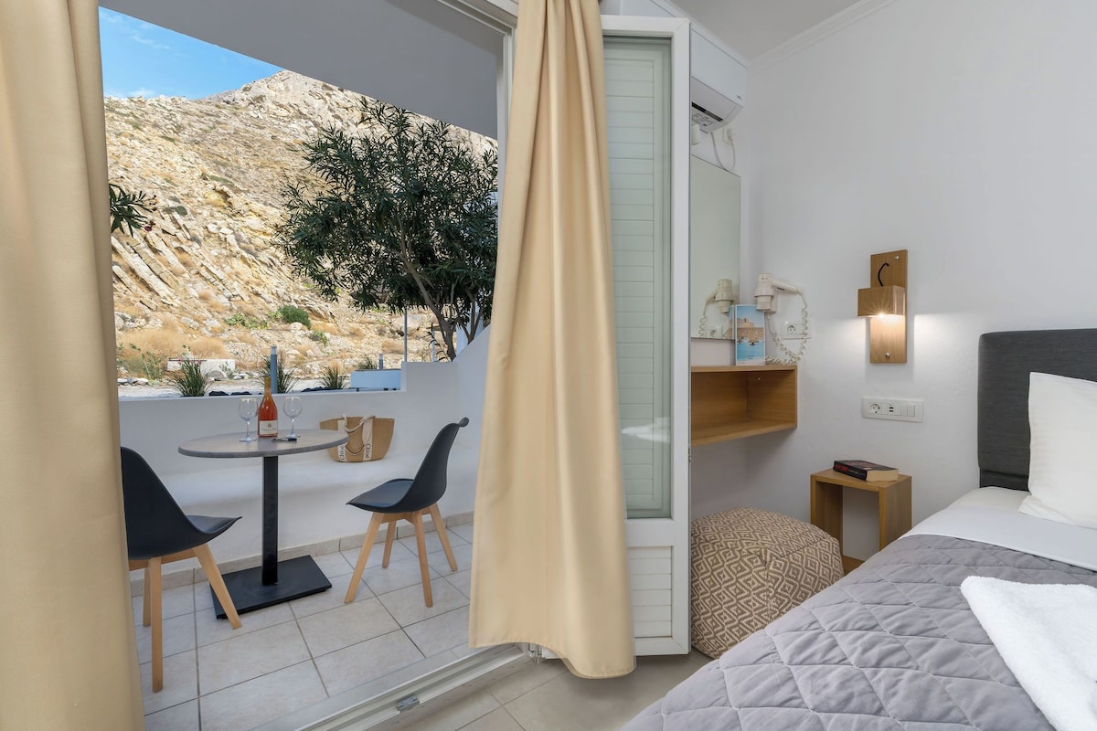 A hotel room with a bed, bedside table, and a small table with chairs outside.