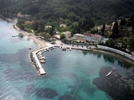 Vista aérea de una zona costera con un puerto deportivo, edificios y una ladera boscosa.